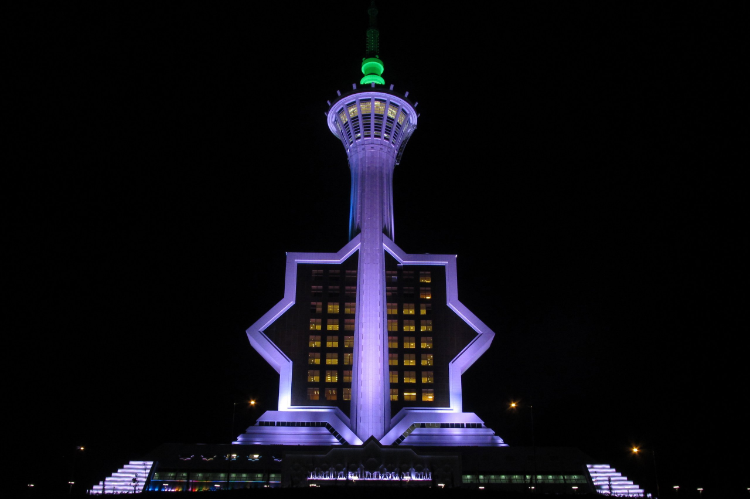 Night view of a tall tower with purple and green lights and a star-shaped building base.