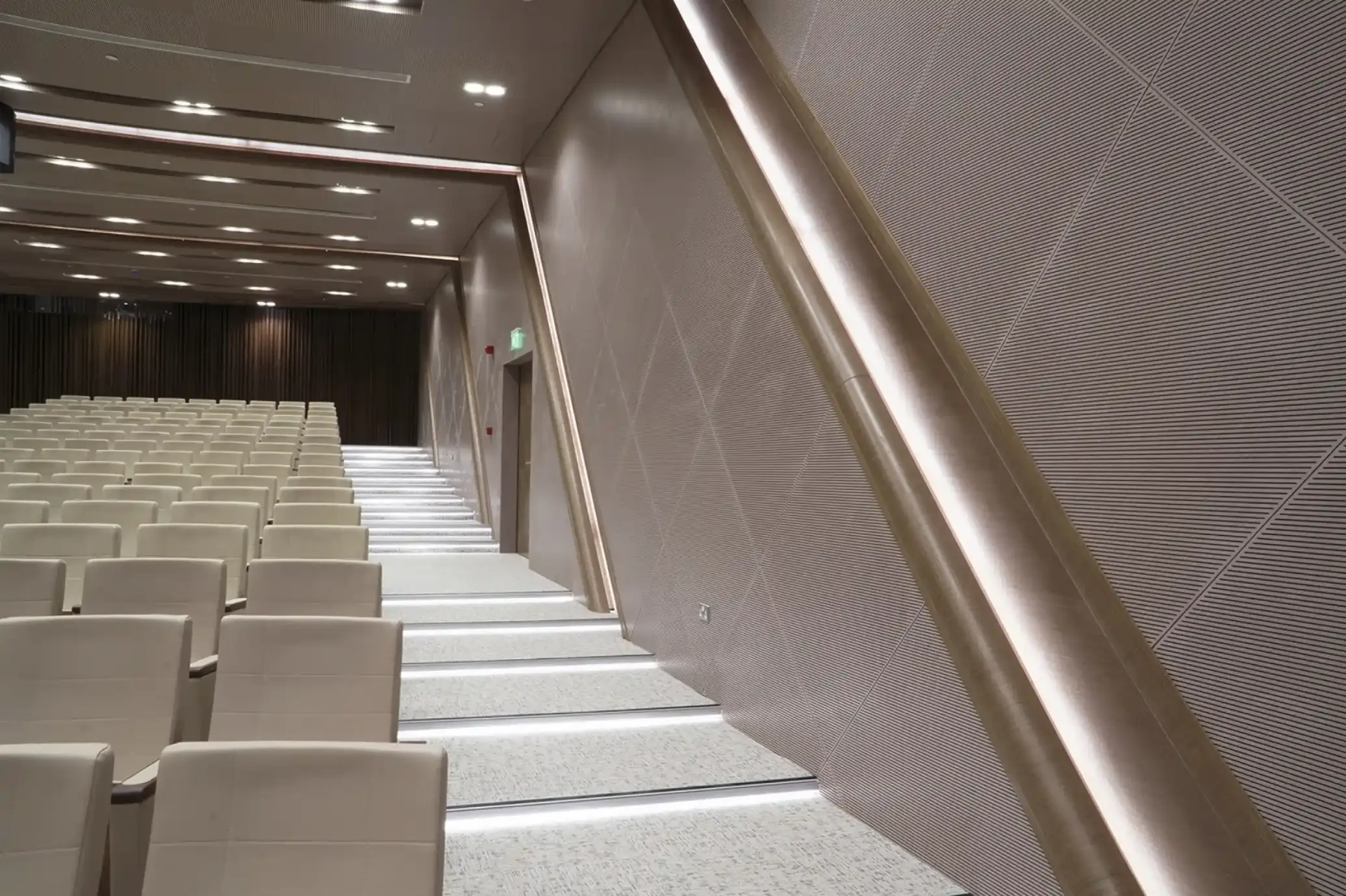 Modern auditorium with beige seats, illuminated stairs, and patterned acoustic wall panels.