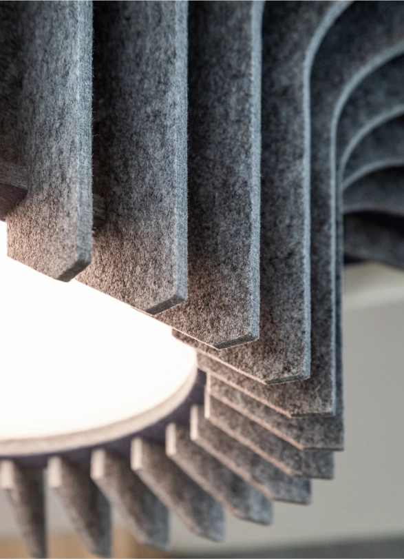 Close-up of a modern circular light fixture with textured grey acoustic panels arranged around the glowing centre.