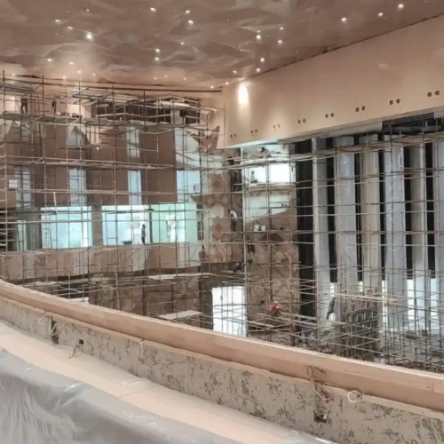 Interior of a large building under construction with extensive metal scaffolding and exposed concrete walls.