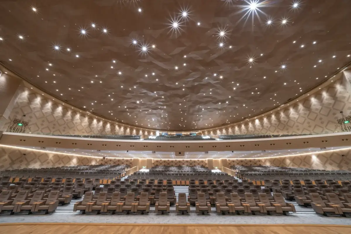 Spacious modern auditorium with multiple rows of brown cushioned seats and a ceiling decorated with numerous small bright lights.