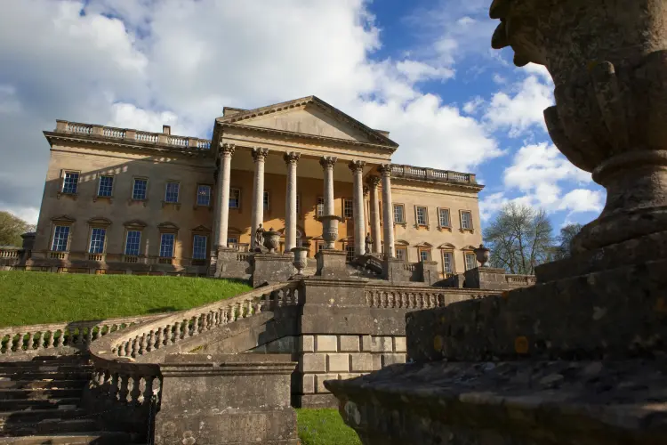 Grand classical mansion with tall columns and stone balustrade under a partly cloudy sky.
