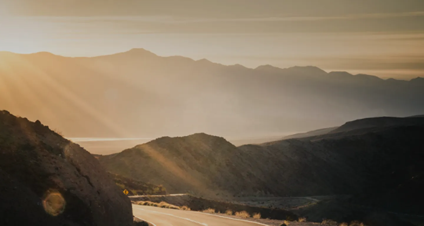 Kinder spielen im Meerwasser am Strand bei sonnigem Wetter mit Bergen im Hintergrund.