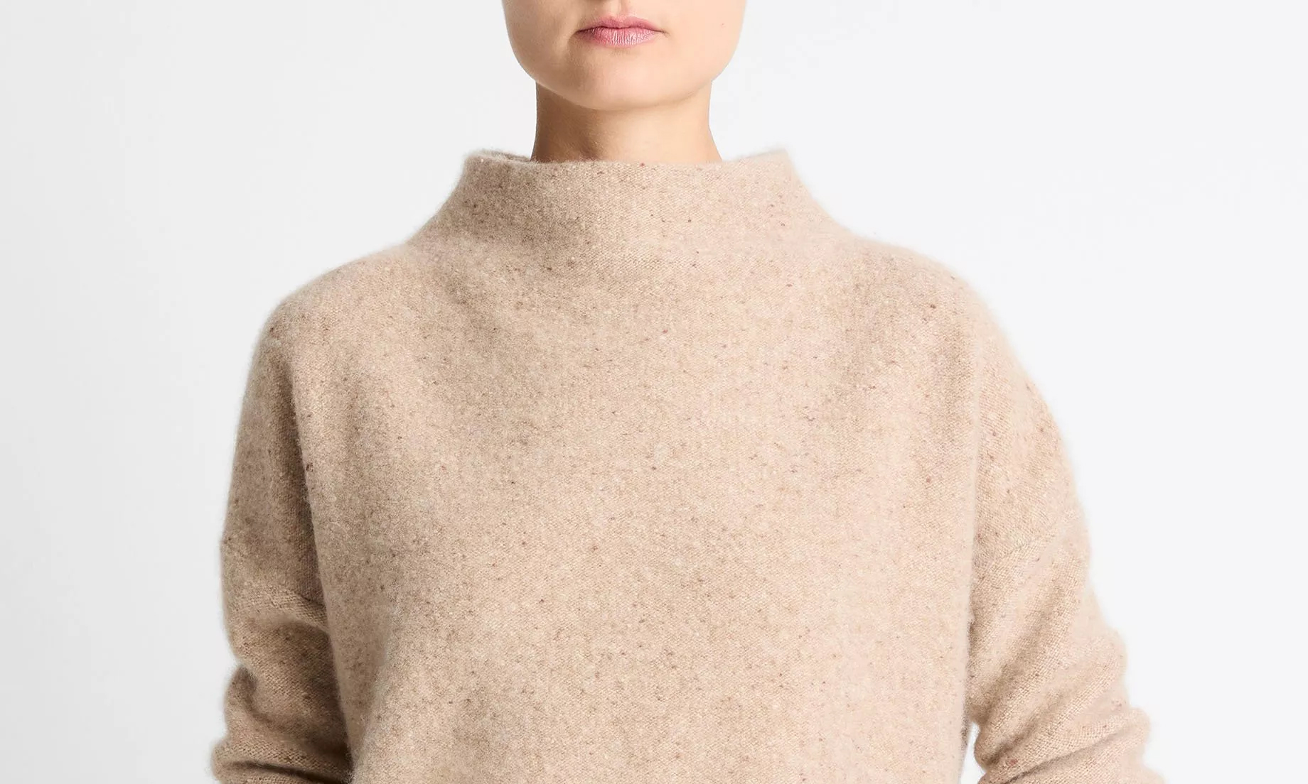 Close-up of a person wearing a beige, high-neck fuzzy sweater with long sleeves against a plain white background.