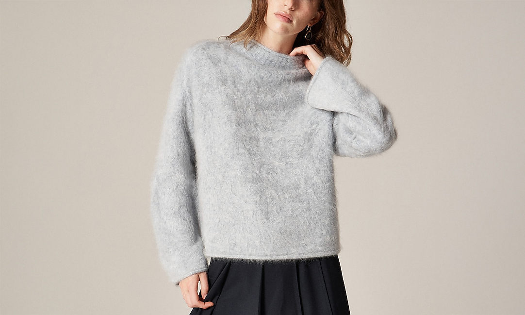 Woman wearing a light grey fuzzy sweater with long sleeves and a high neck.