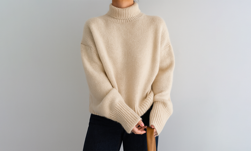 Person wearing a beige turtleneck sweater and dark pants, holding a brown strap or handle.