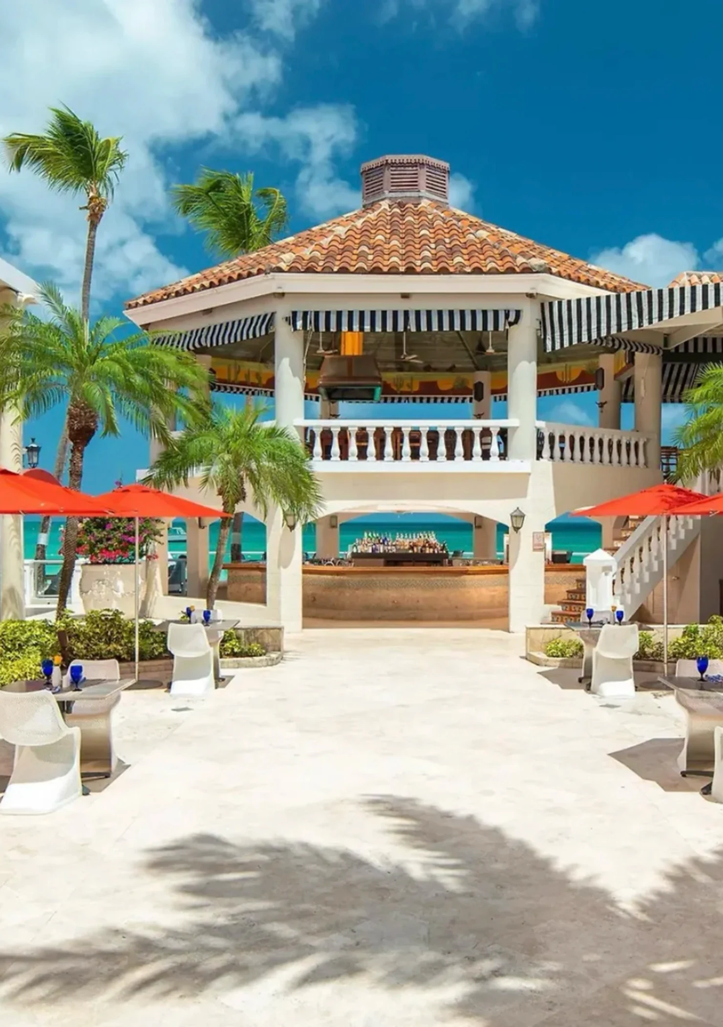 Tropical beach resort with white gazebo, red umbrellas, and palm trees