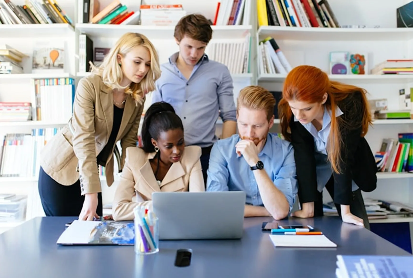 Five professionals gathered around a laptop in a modern office, collaborating on a project.