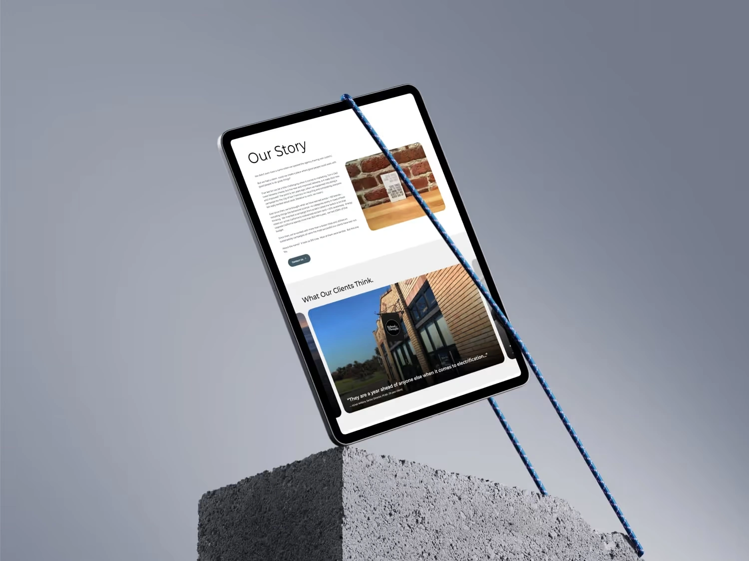 Tablet displaying a webpage titled 'Our Story' and client testimonials, suspended by two blue ropes above a textured concrete block against a gray background.