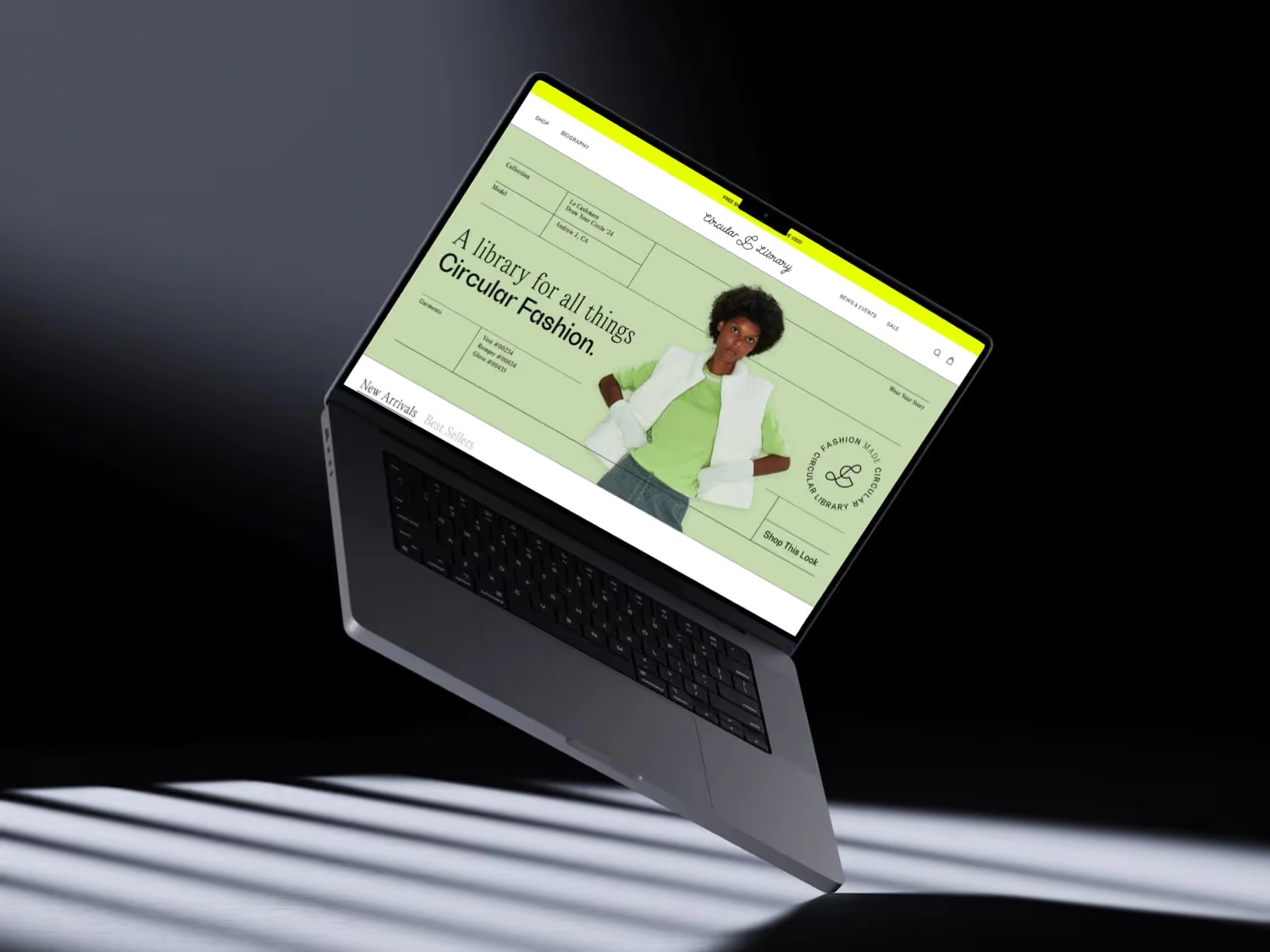 Open laptop floating in dark space displaying a fashion website with a model in a green shirt and white vest.