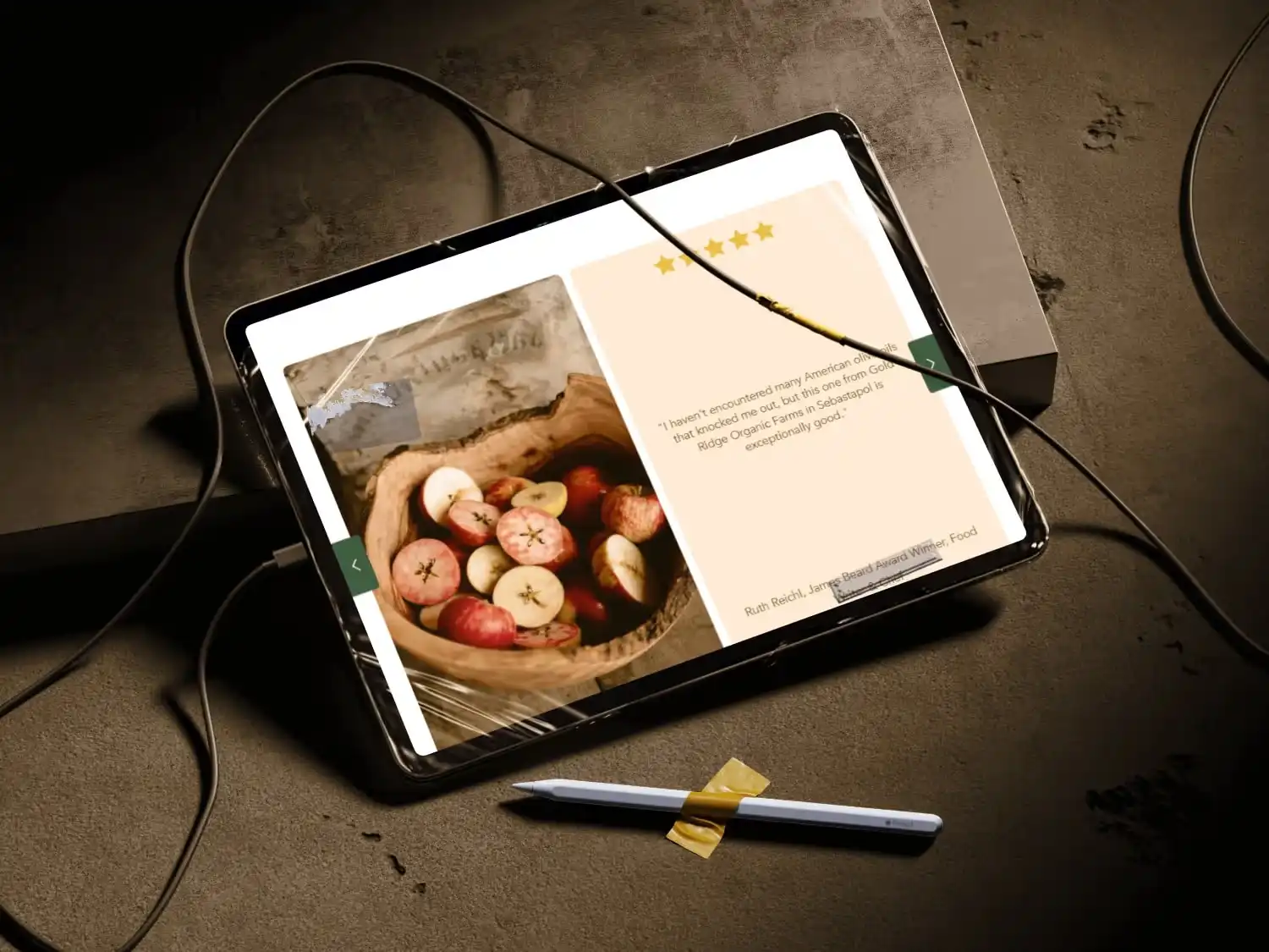 Tablet on a textured surface displaying a review with a basket of sliced apples and a five-star rating, a stylus taped below it, and charging cables connected.