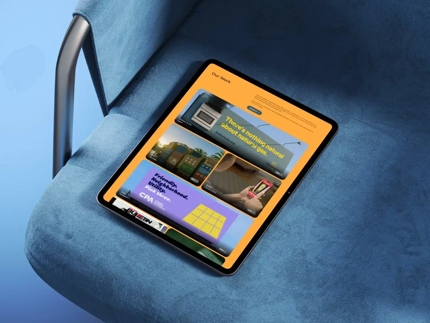 Tablet displaying a webpage with colorful sections about natural gas and community utilities, placed on a blue fabric chair.