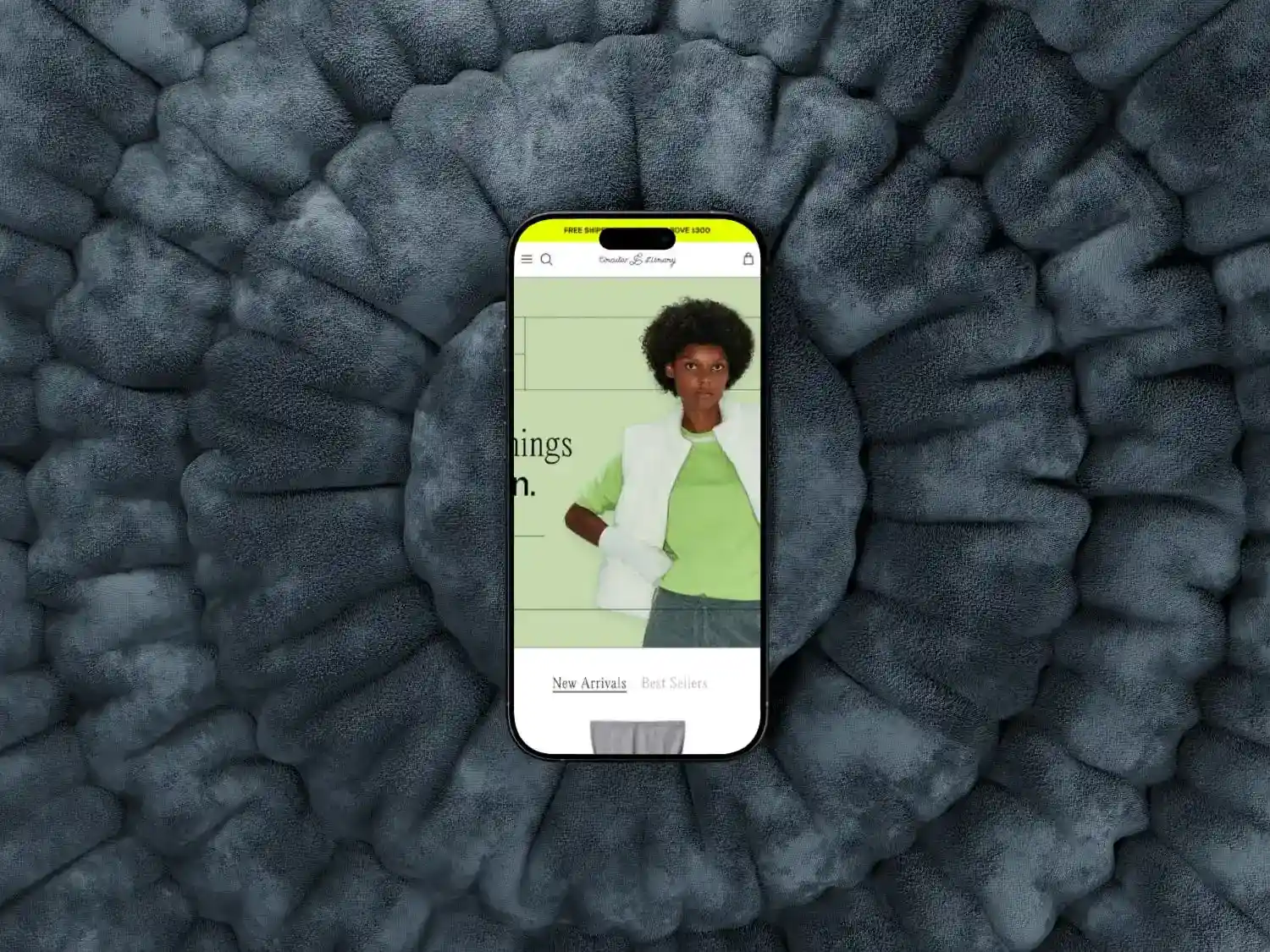 Smartphone displaying a fashion website with a model wearing a white vest and green top on a textured dark grey background.