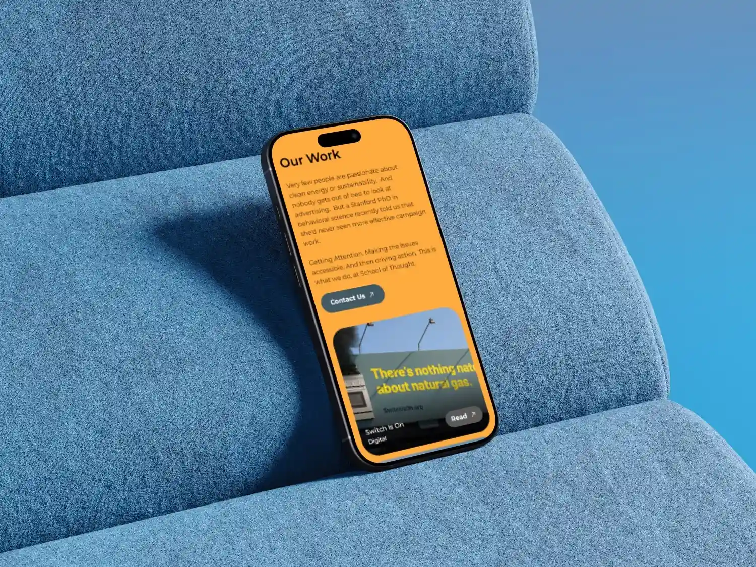 Smartphone on blue textured fabric surface displaying a webpage titled 'Our Work' with text about clean energy and sustainability, and a section mentioning natural gas.