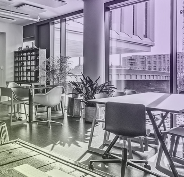 Modernes Büro mit großen Fenstern, mehreren Stühlen, Tischen und grünen Pflanzen.