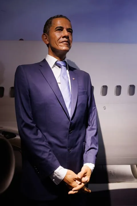 Wax figure of Barack Obama in a blue suit standing before an airplane backdrop at WAX Museum of Legends Colmar