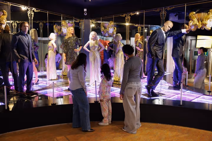 Trois visiteurs observant des mannequins habillés élégamment dans une vitrine éclairée avec des miroirs et des lumières LED roses.