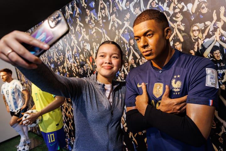 Une jeune femme prend un selfie avec une statue de cire d'un joueur de football français en maillot bleu.