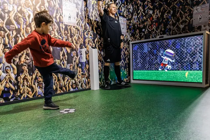 Enfant au jeu de penalty interactif de la salle football, près d’un arbitre de cire — Wax of Legends Colmar