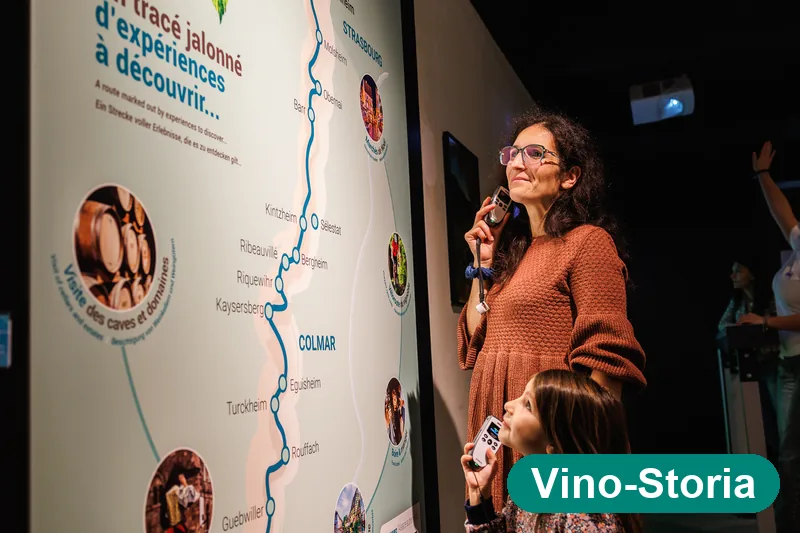 Visitatrice con l'audioguida davanti alla mappa della strada dei vini d'Alsazia — Vino-Storia Colmar