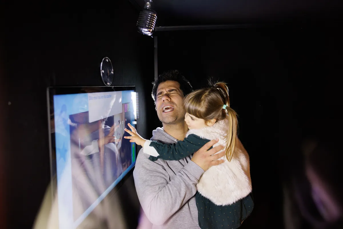 Ein Vater und seine Tochter singen am interaktiven Karaoke des Wax of Legends, Mikrofon vor dem Touchscreen