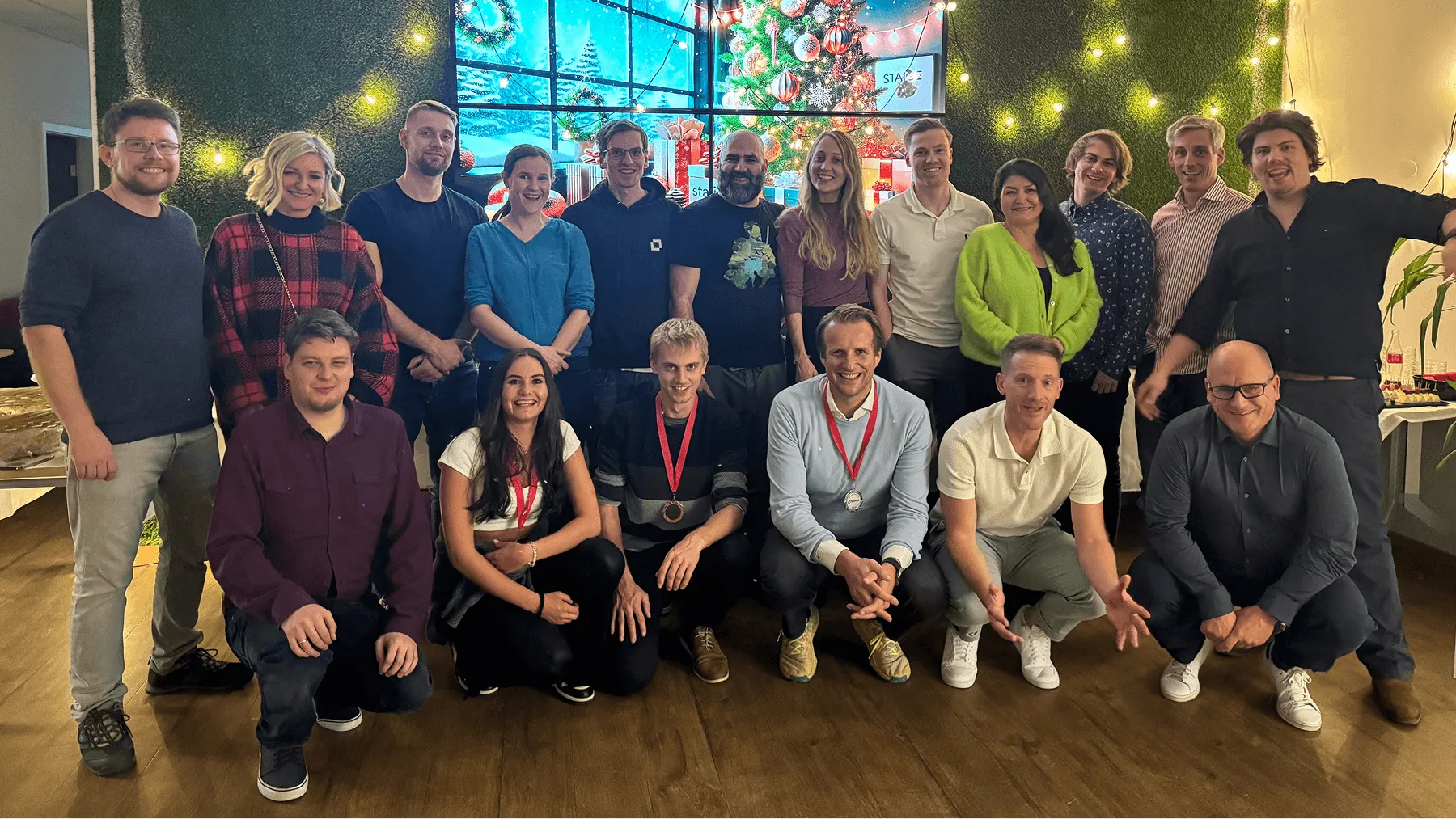 Staige team poses in front of Christmas tree with string lights and gifts.
