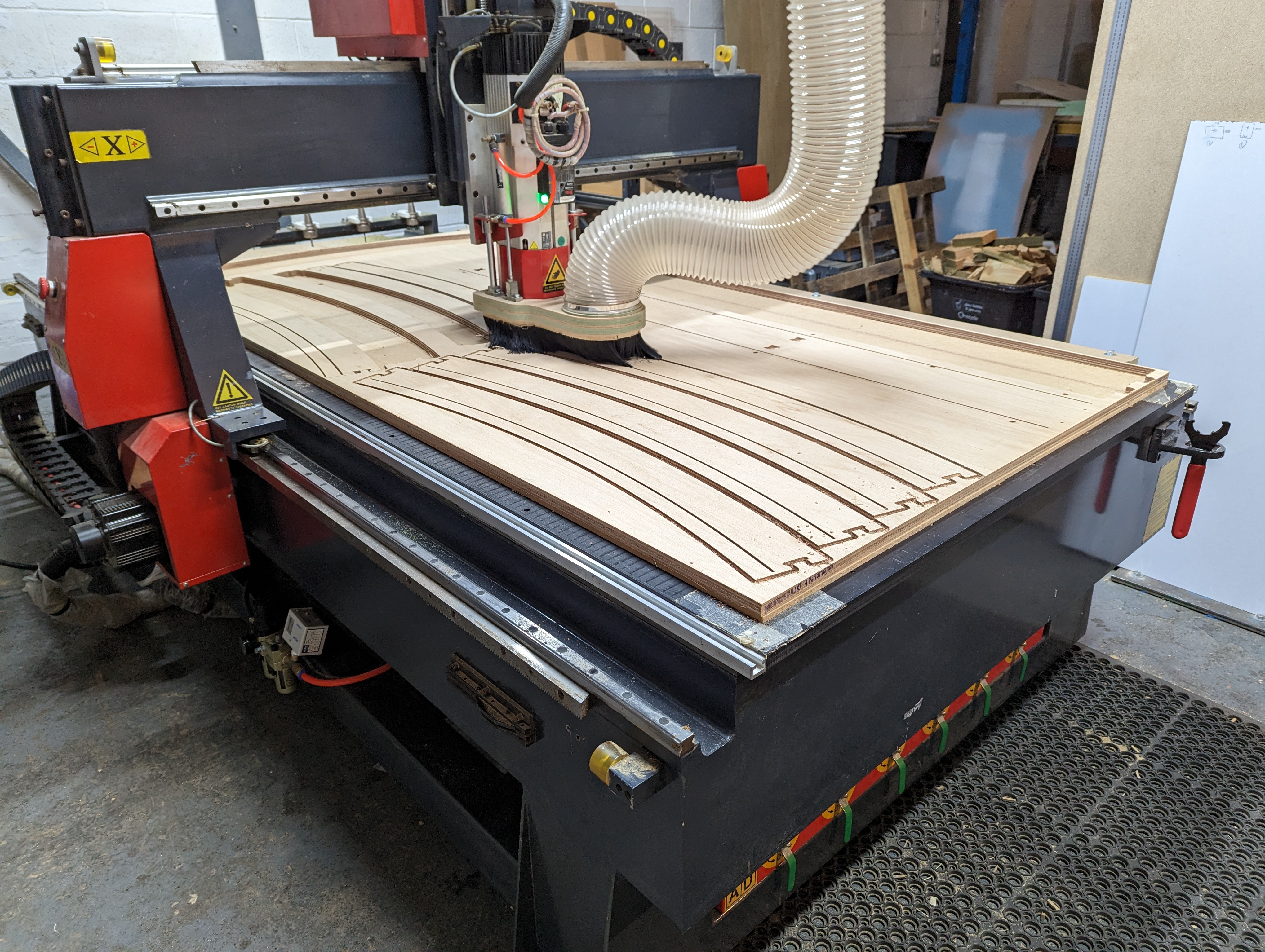 Large CNC machine cutting curved grooves into a wooden board in a workshop.