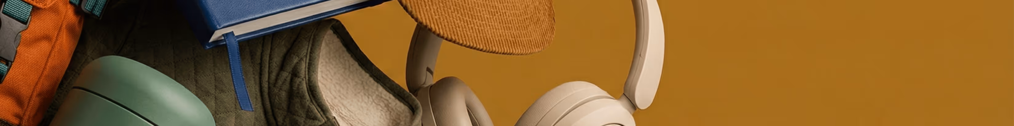 Assorted lifestyle items including a backpack, notebook, cap, headphones, and a green travel tumbler on a warm mustard background.
