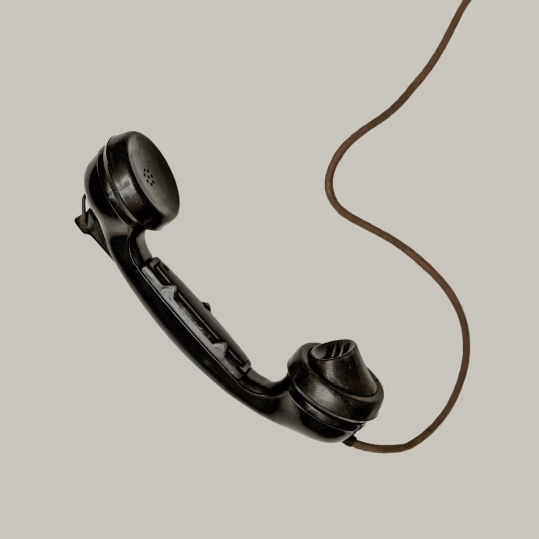 A phone hanging off the reciever on a sage green background.