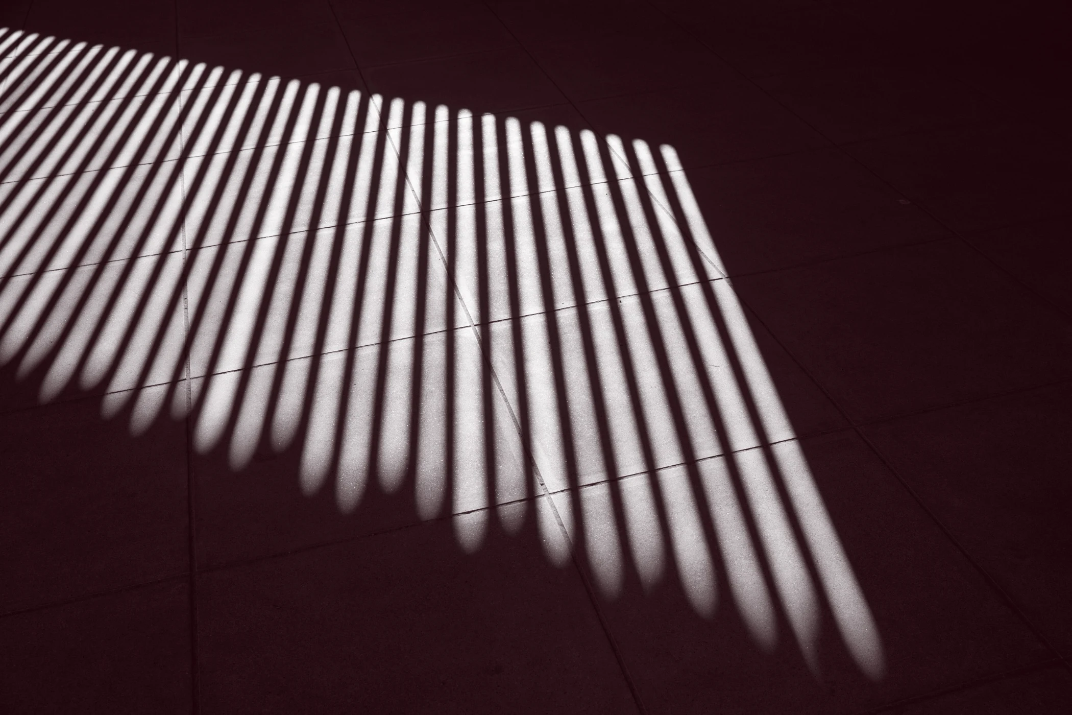 Shadow pattern of evenly spaced vertical bars cast on a tiled floor.