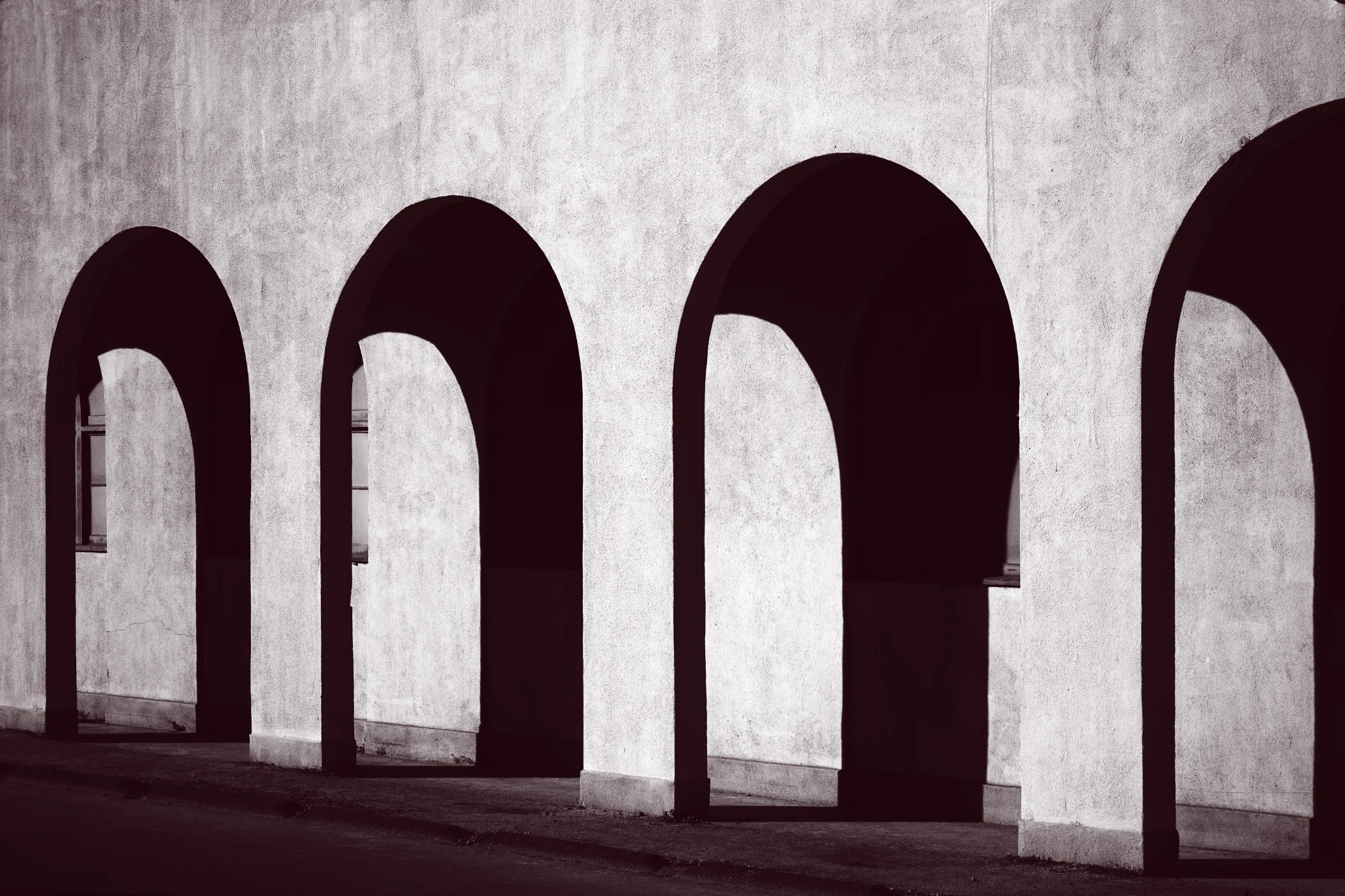 Black and white photo of a row of four large, empty arches casting deep shadows on a textured wall.
