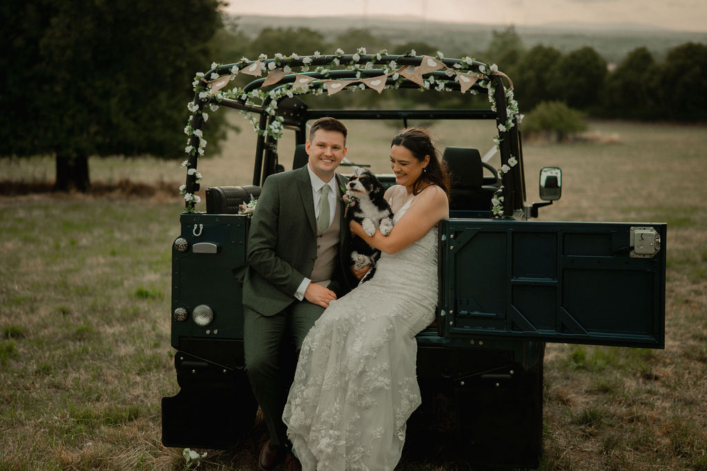 A blue land rover decorated for a wedding with a newly wed couple