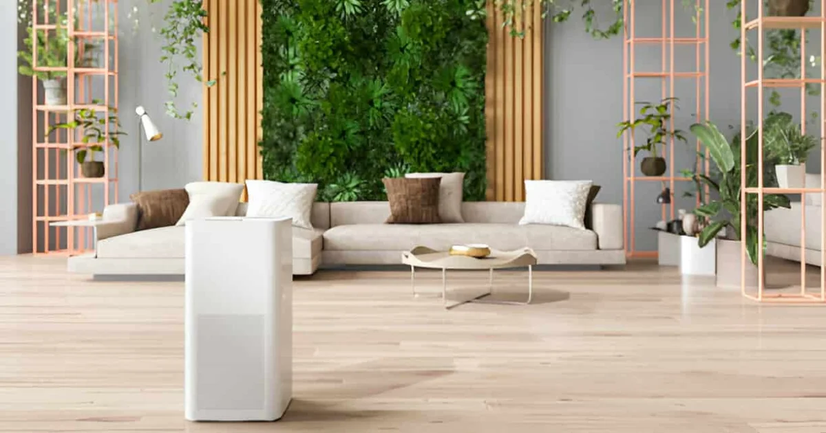 Modern living room with a beige sectional sofa, greenery wall decor, indoor plants, and a white air purifier in the foreground.