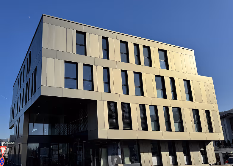 Modernes mehrstöckiges Gebäude mit grauer Fassade und großen Fenstern unter klarem blauem Himmel.