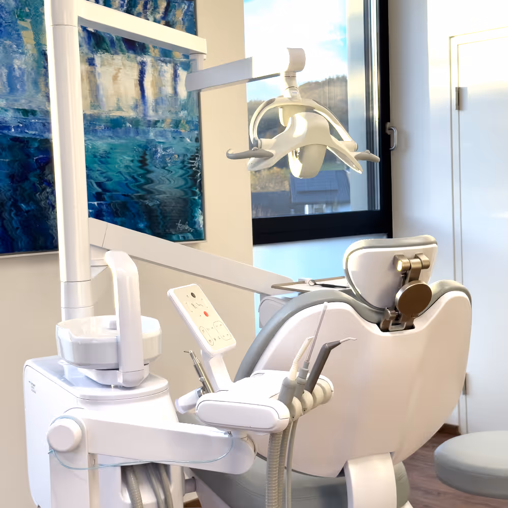 Moderner Zahnbehandlungsstuhl mit Zahnärztelicht und Instrumenten in einer hellen Praxis mit Fenster und Kunstbild.