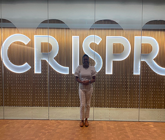 Person standing in front of large illuminated letters spelling CRISPR on a wooden-paneled wall.