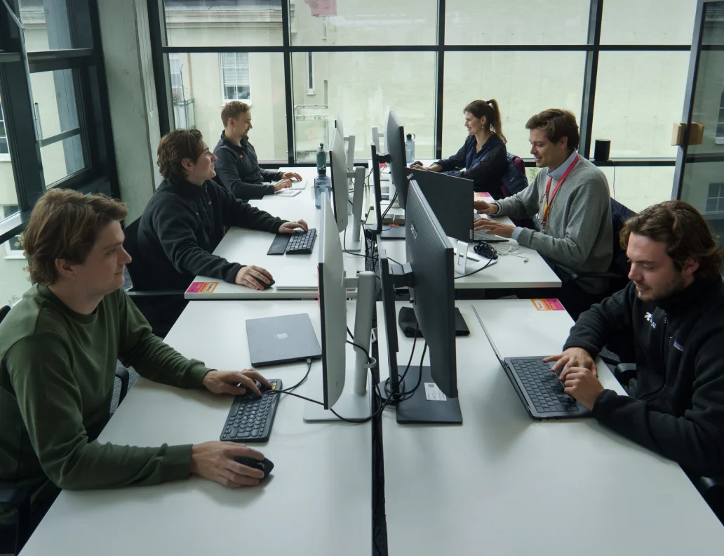 Three colleagues in a modern office, one woman holding a laptop and a man showing data on a tablet during a discussion.