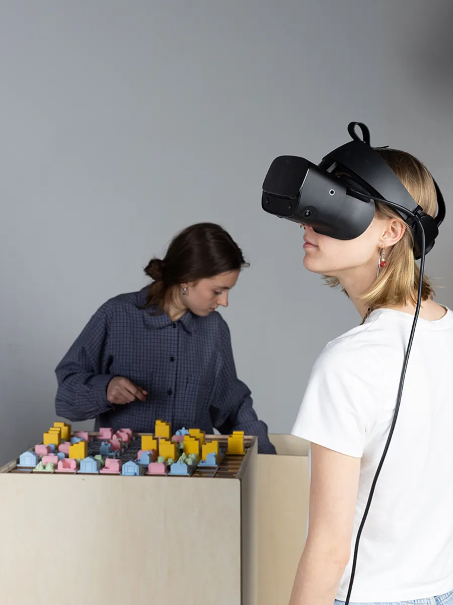 a person wearing VR glasses with another person playing with the Urbanova grid in the background.