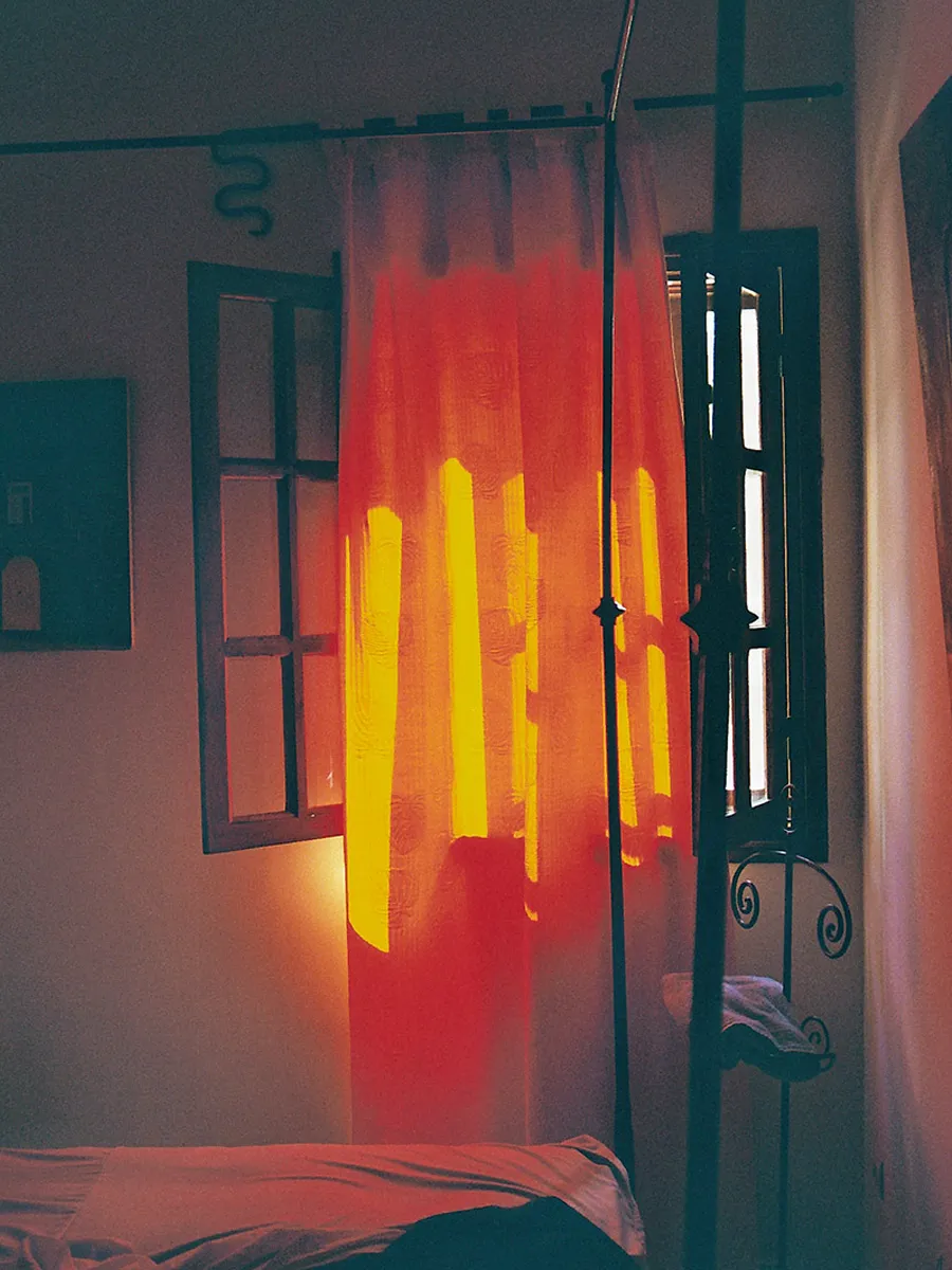 Sun shines through a red curtain in front of a window and illuminates the room.
