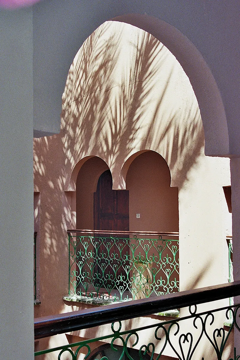The view from one moroccan balcony to another with shadows of palm trees playing on the walls with the light.