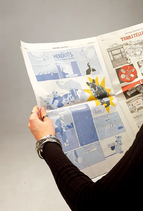 A person holding a newspaper showing Volume 1 of HeroRats the comic.