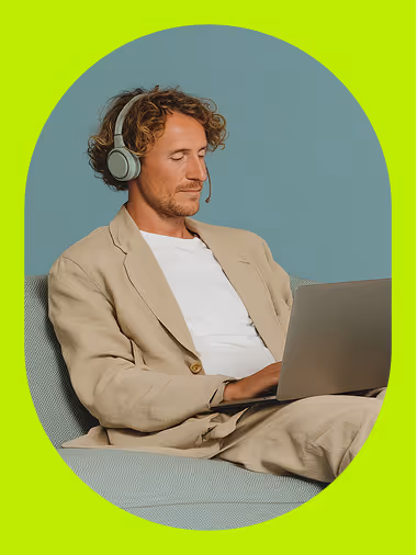 A professionally dressed man using a laptop with headphones while sitting on a sofa, highlighting remote hiring efficiency and modern workplace flexibility.