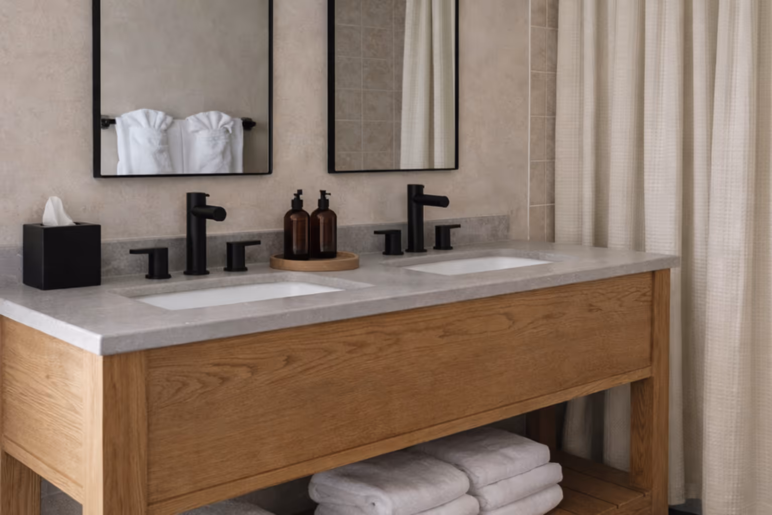 Modern bathroom with a wooden vanity holding white folded towels, a large mirror, black fixtures, beige tiled shower with a white curtain, and gray tiled floor.