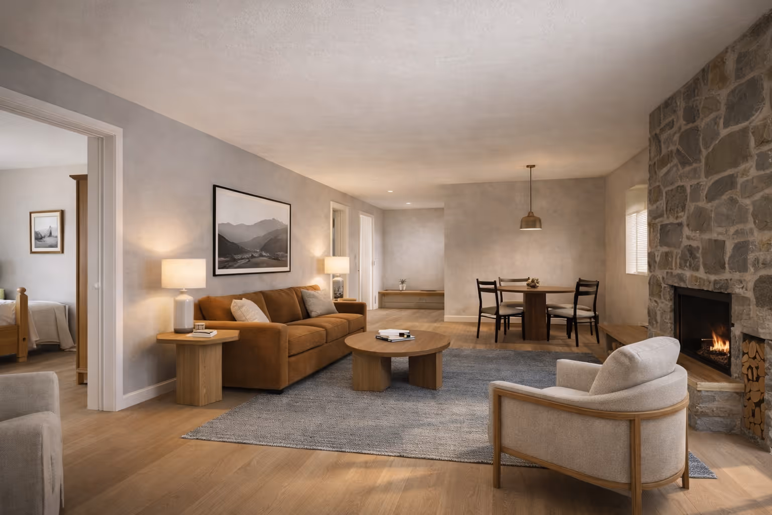 Modern living room with a brown sofa, beige armchair, round wooden coffee table on a gray rug, dining table with four chairs, and a stone fireplace.