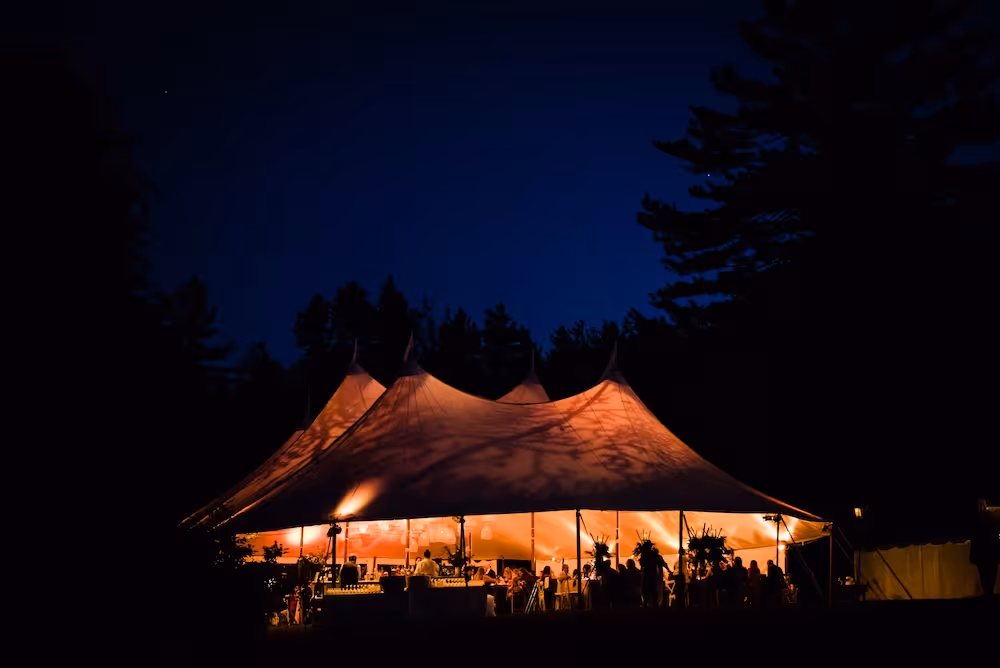 Large event tent illuminated from inside at night with people and tables visible.