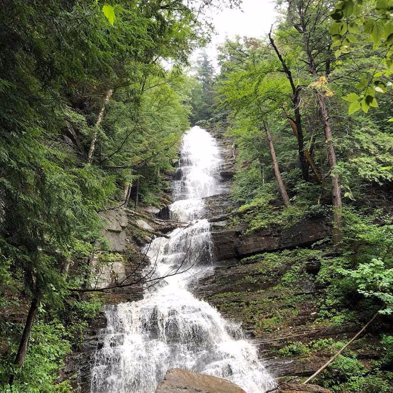 Tall cascading waterfall surrounded by dense green forest and rocky cliffs.