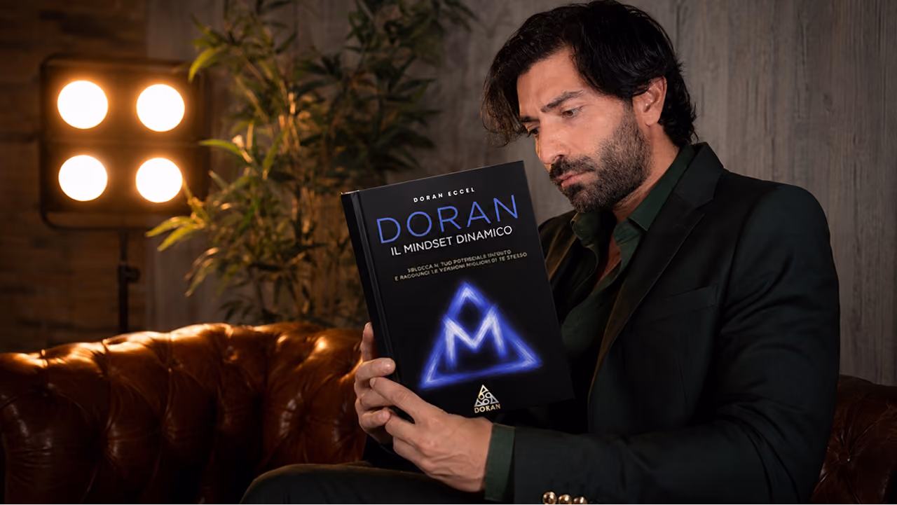 Man sitting on leather couch reading a book called 'Doran The Dynamic Mindset'.