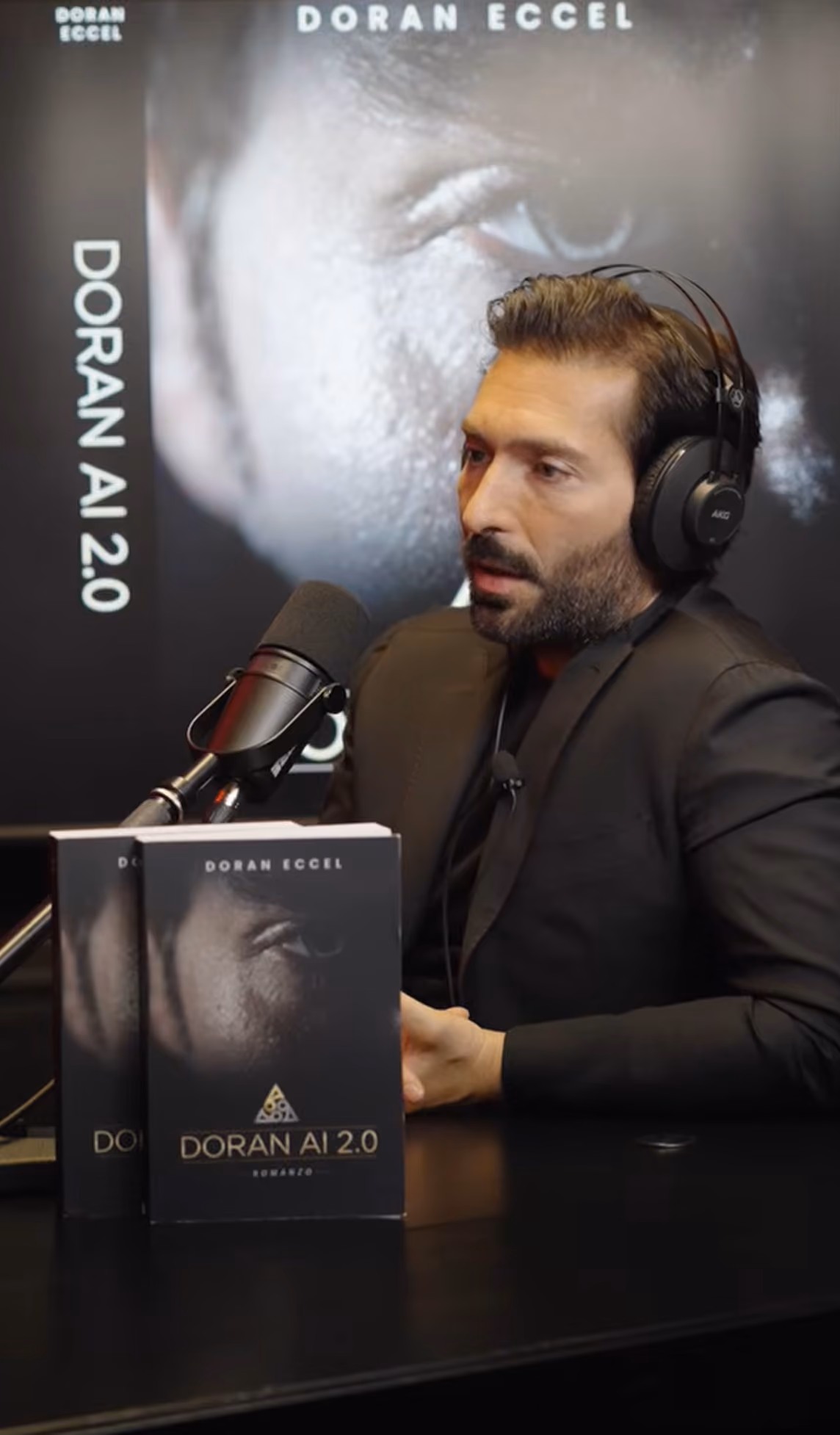 Man with headphones speaks into the microphone in front of Doran AI 2.0 books in a podcast or interview.