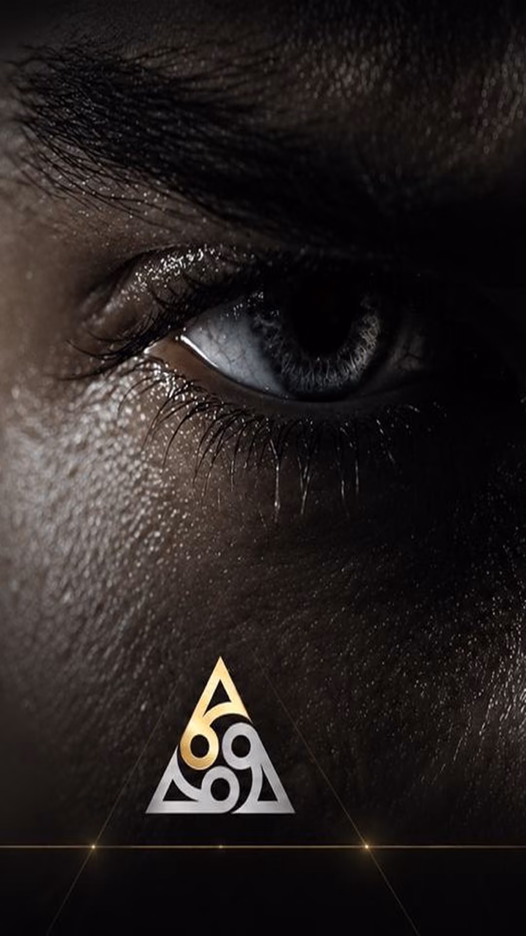 Close-up of a blue eye and eyebrow amid textured dark skin with a gold and white triangular symbol below.