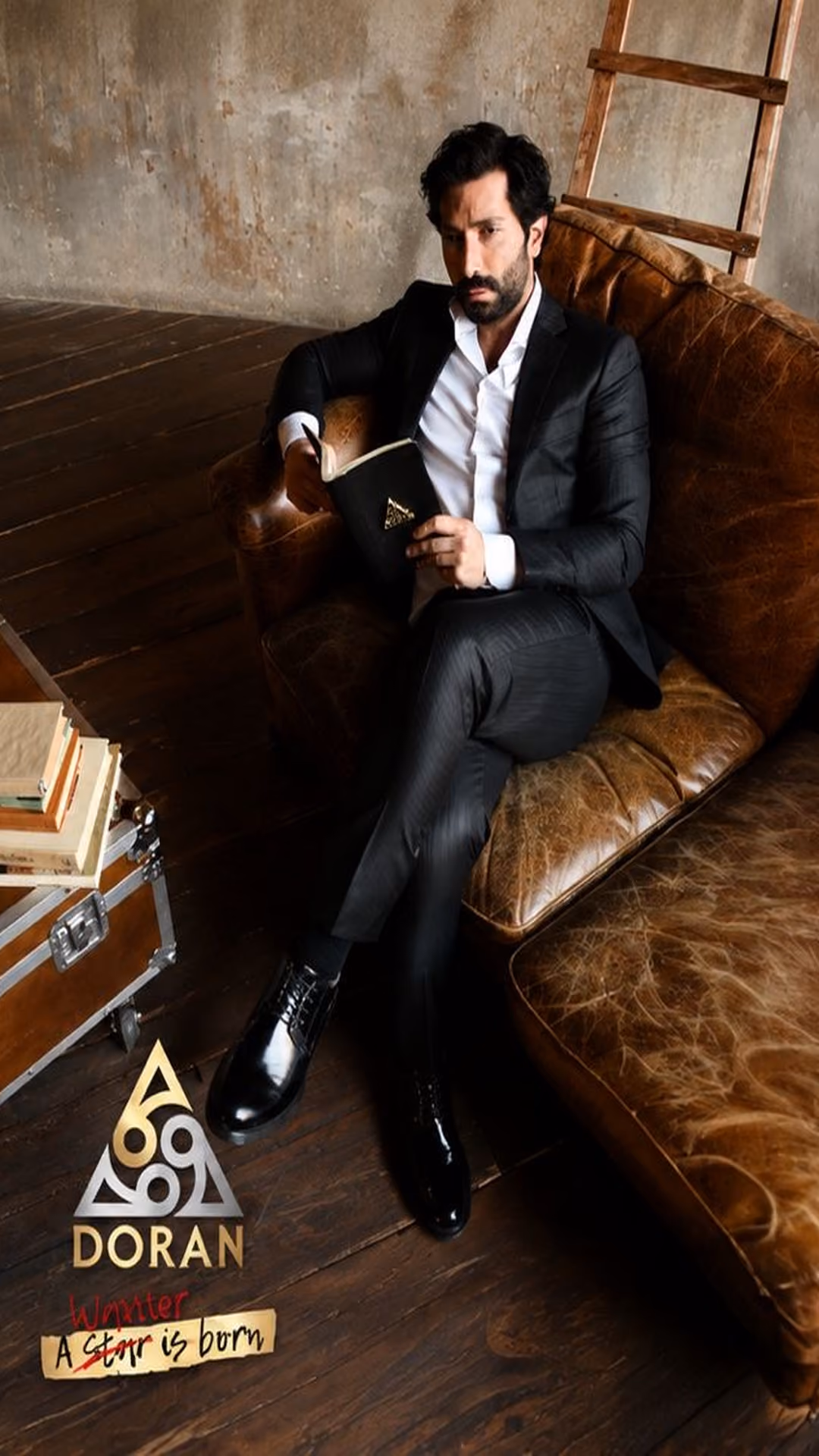 Man in dark suit sitting on brown leather couch with book in hand in rustic room.